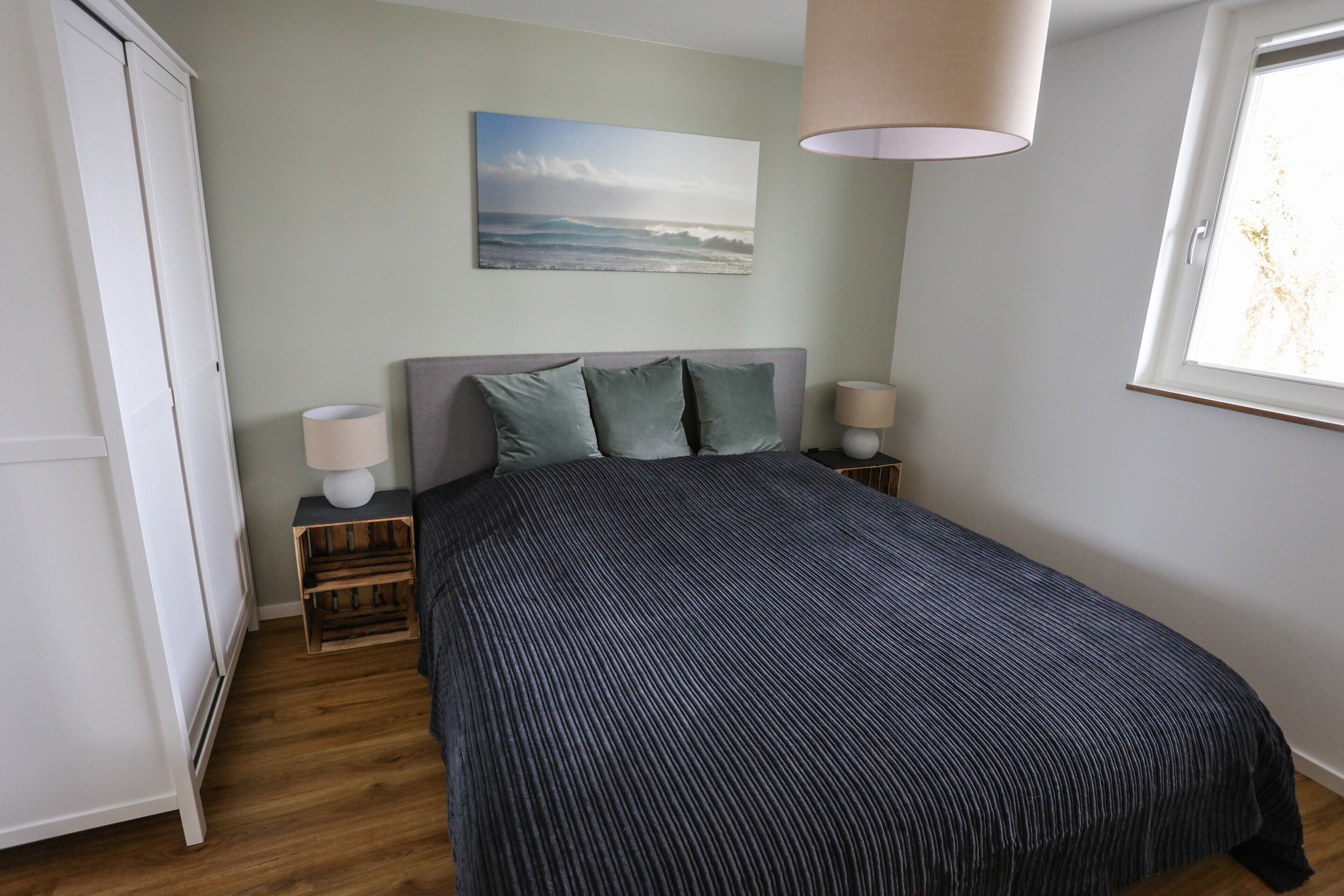 Une chambre à coucher avec un lit, des tables de chevet, une lampe, un tableau et une fenêtre.