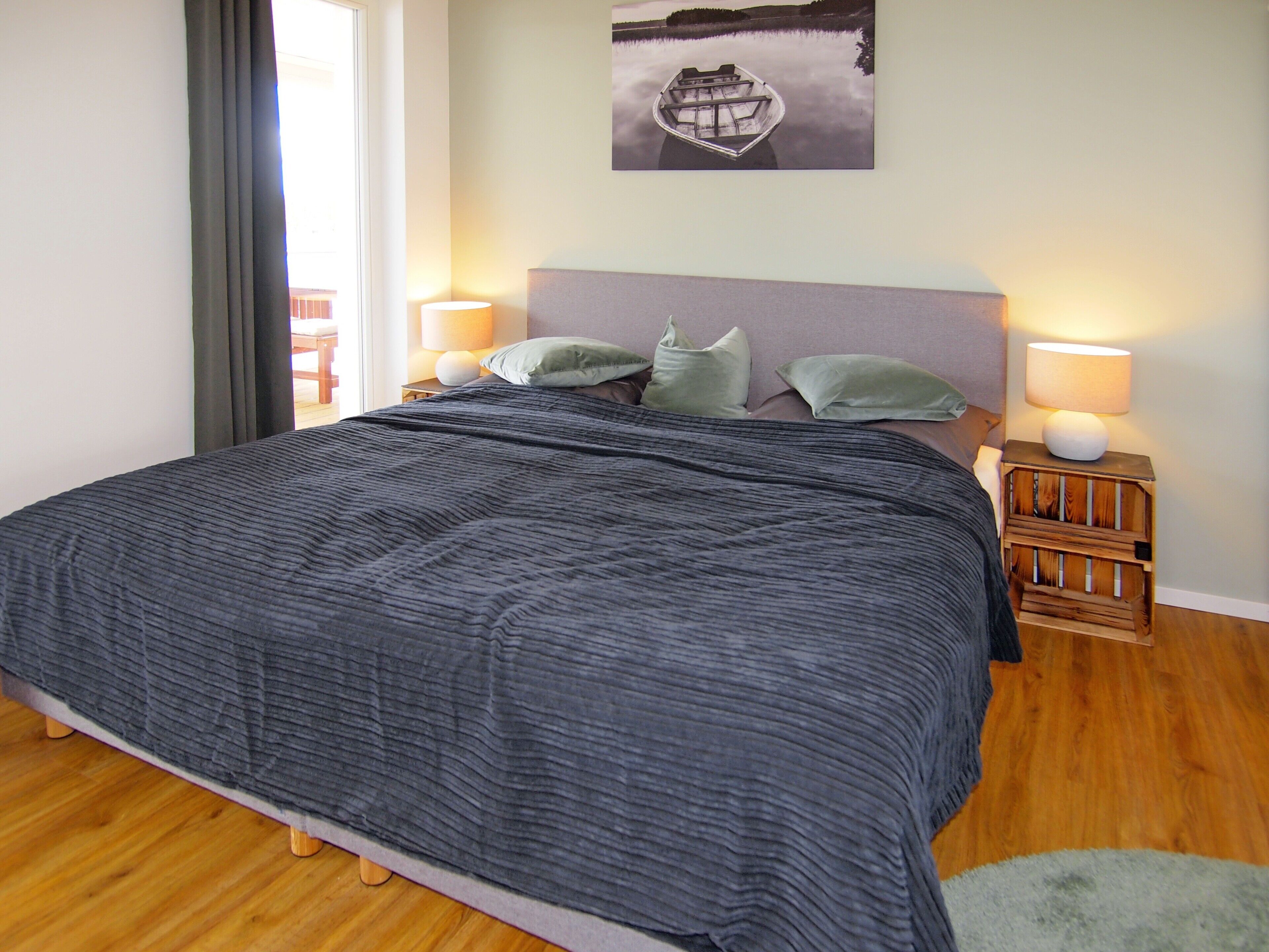A bedroom with a large bed, two bedside lamps, a nightstand with a lamp, a framed picture on the wall, and a window with curtains.