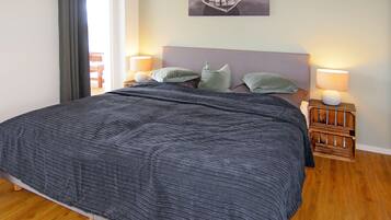 A bedroom with a large bed, two bedside lamps, a nightstand with a lamp, a framed picture on the wall, and a window with curtains.