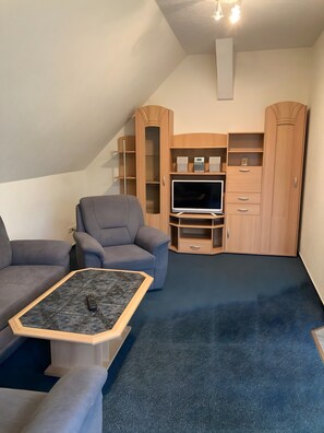 Un salon avec un téléviseur, deux canapés gris, une table basse et des meubles en bois.