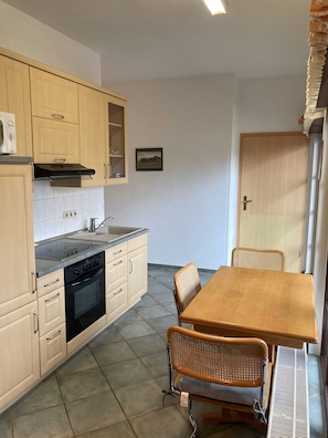 Une cuisine équipée d’une cuisinière, d’un four et d’un évier, une table à manger avec des chaises et une porte.