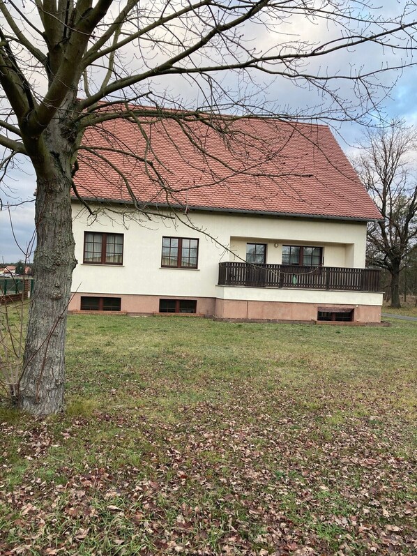 A two-story building with a red-tiled roof, a balcony with a black railing, and a grassy yard. - Apartment 'Jungfernteich' with Balcony and Wi-Fi (Frauendorf)