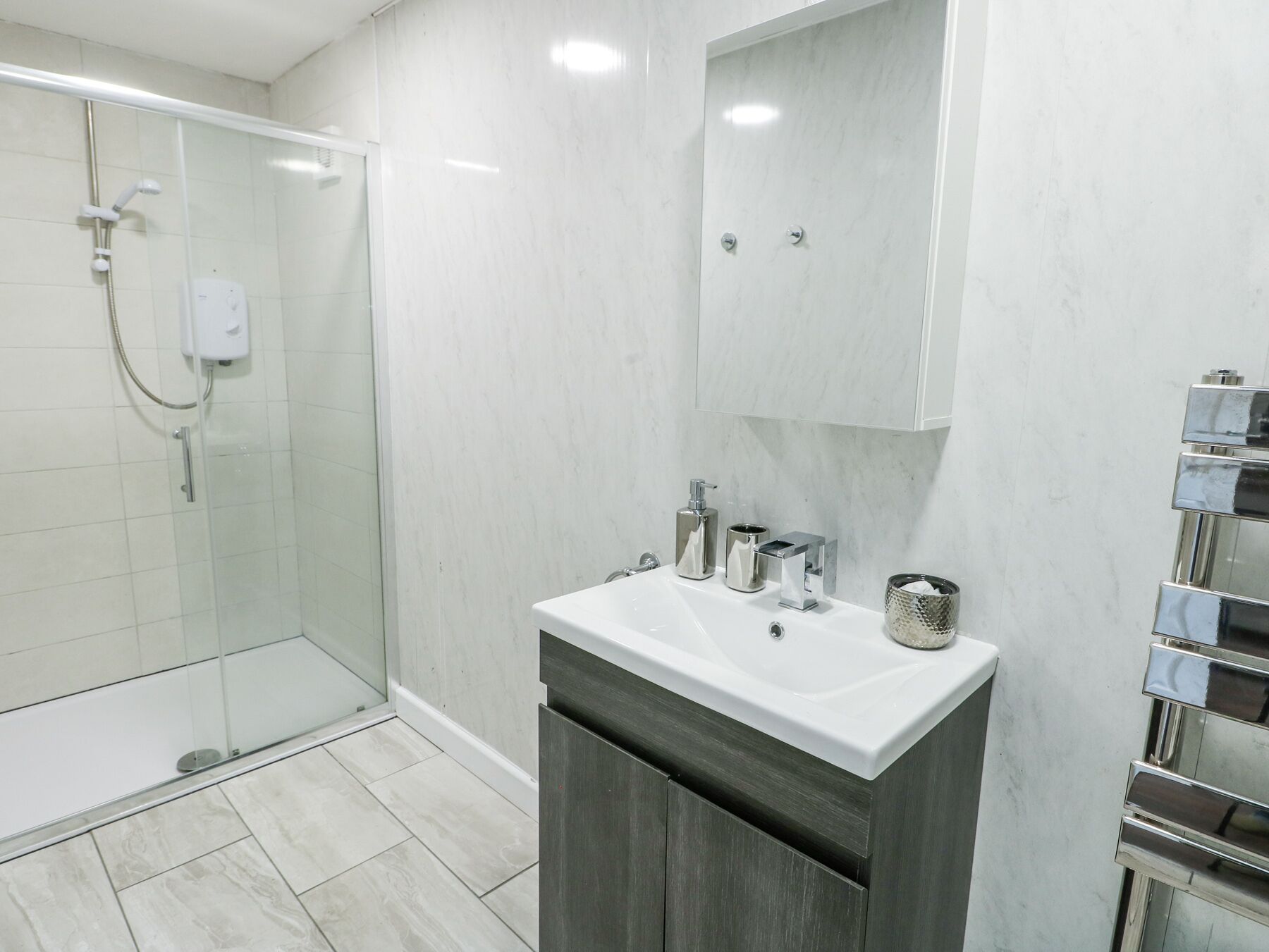 Un baño moderno con cabina de ducha de vidrio, un lavamanos blanco con accesorios de cromo y suelo de baldosas de mármol.