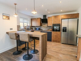 A modern kitchen with a wooden table and bar stools, stainless steel appliances, and a built-in oven.