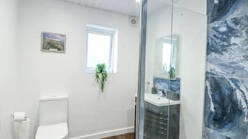 A modern bathroom with a toilet, a glass-enclosed shower, a sink, and a window with a plant.