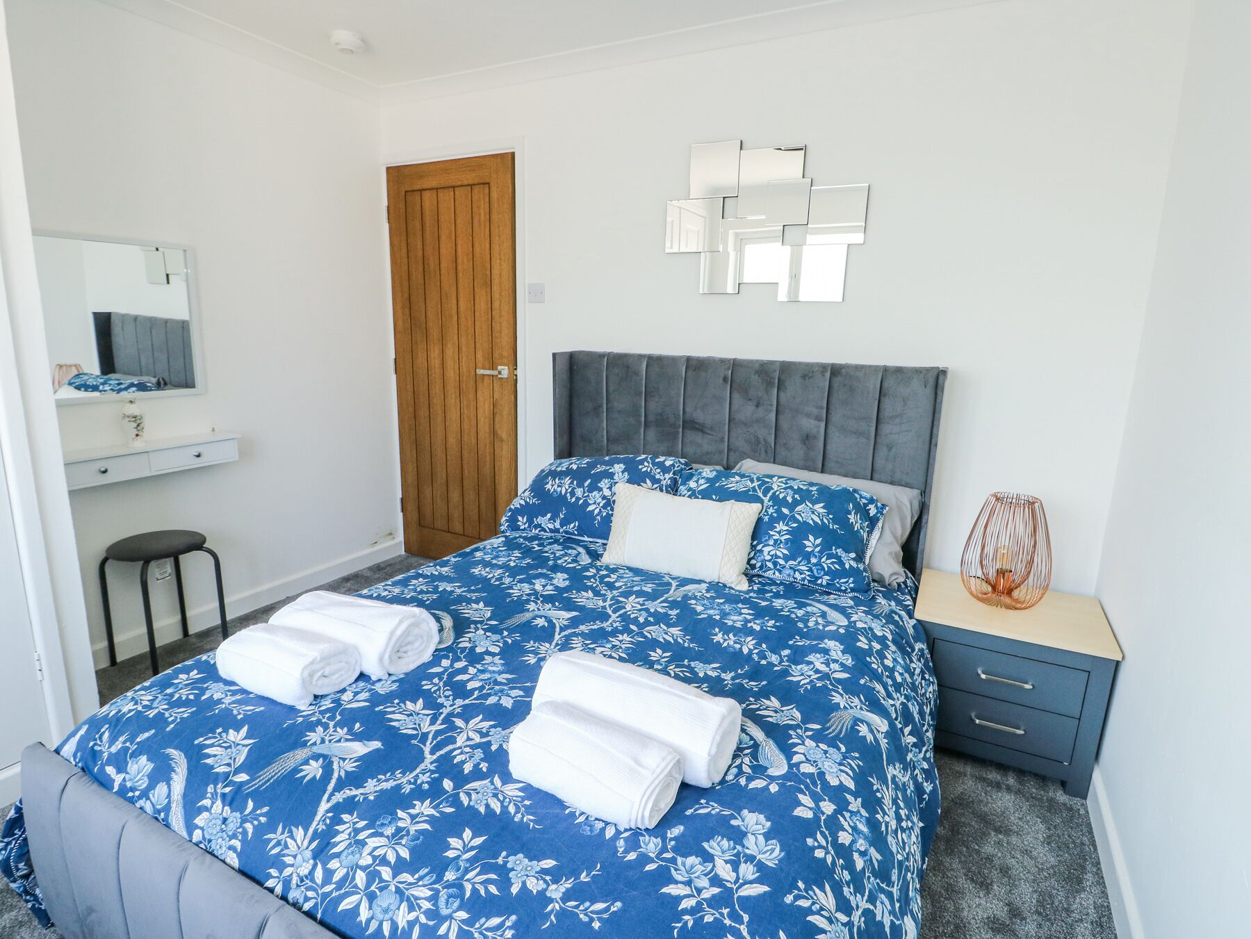 Une chambre à coucher avec un lit, une porte en bois, un miroir, une table de chevet et une chaise.