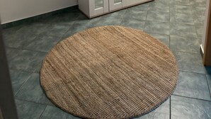 Una habitación con un armario blanco, un pequeño banco y un tapete tejido sobre un suelo de baldosas.