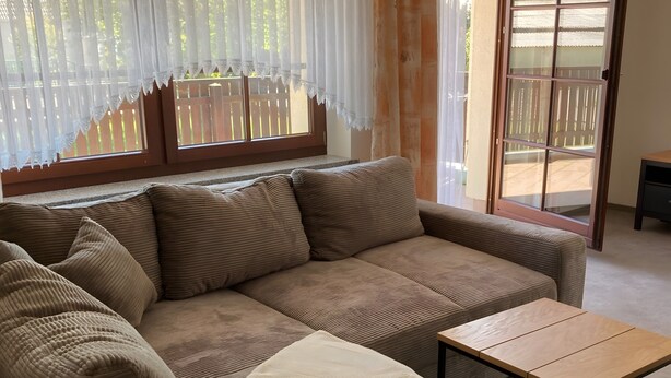 Un salón con un sofá modular, una mesita de madera y un ventanal corredero que da a un espacio exterior.