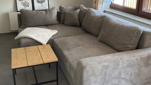 Sala de estar con un sofá modular, una pequeña mesa de madera e impresiones botánicas enmarcadas en la pared.