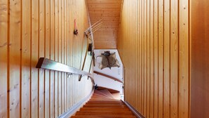 Een houten interieur met een spiraaltrap, een bontjas aan de muur en een plafondlamp.