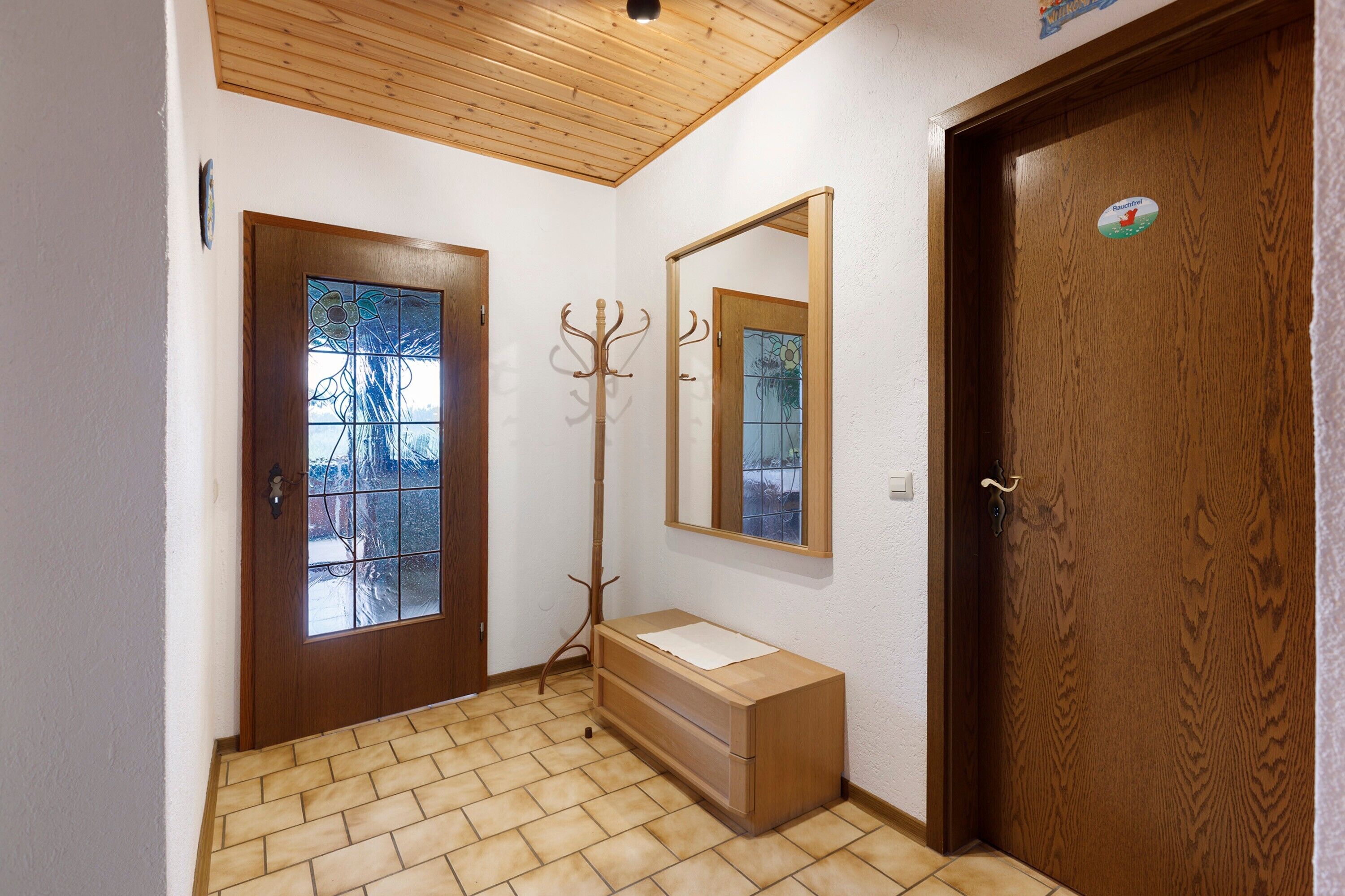 Ein Flur mit Holztür, Kleiderhaken, Spiegel und einem kleinen Holzschrank.