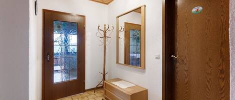 Ein Flur mit Holztür, Kleiderhaken, Spiegel und einem kleinen Holzschrank.