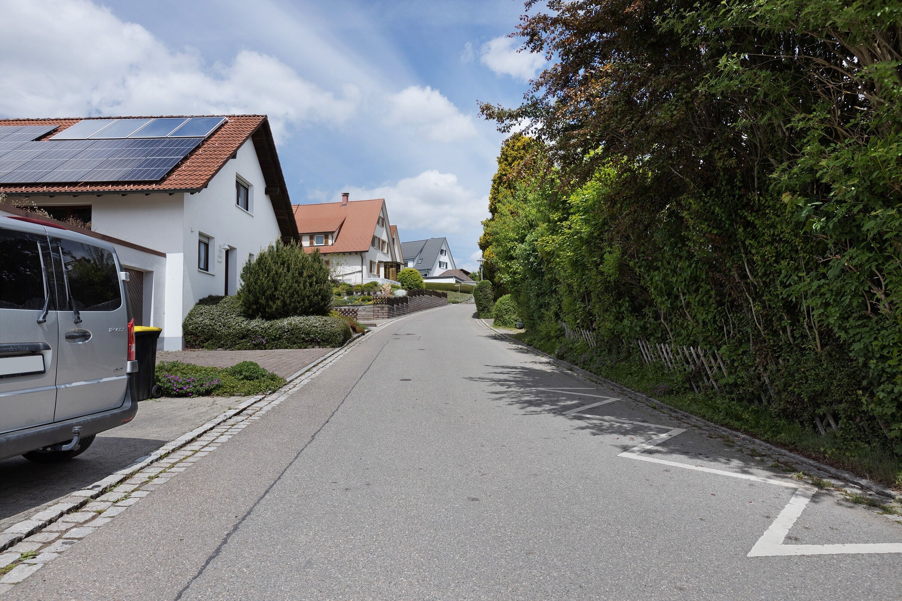 Une rue résidentielle bordée de maisons, avec une voiture garée et des panneaux solaires sur l’un des toits.