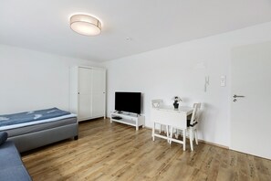 A modern, minimalist room with a bed, a TV, a desk, and a chair.