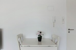 A white table with a potted plant, two white chairs, a white door with a keyhole, and a wall socket.