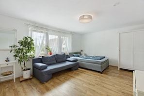 Ein modernes Wohnzimmer mit einer Couch, einem kleinen Tisch, einer Zimmerpflanze, einem Bett und einem Kleiderschrank.