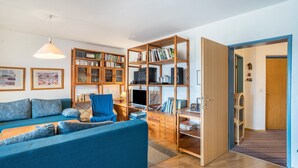 A living room with a blue sofa, wooden bookshelves, a television, and a desk. - Apartment 'Terrassenpark 160' with Mountain View, Balcony and Wi-Fi (Schonach)