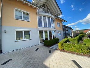 Een gebouw met twee verdiepingen, een balkon, grote ramen en een geplaveid pad.