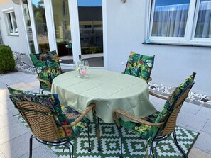 Een ronde tafel met een groene tafelkleed, omringd door rieten stoelen met bloemenmotieven, op een vloer met een patroon.