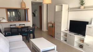 A modern living room with a sofa, dining table, chairs, a TV, and a small cabinet. - 2 bedroom apartment in the Oasis complex (Roquetas de Mar)