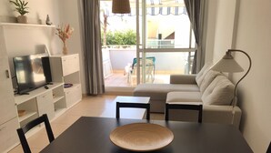 A modern living room with a TV, sofa, dining table, chairs, and a lamp. - 2 bedroom apartment in the Oasis complex (Roquetas de Mar)