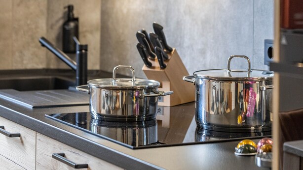 Une cuisine équipée d’une plaque de cuisson à induction sur laquelle reposent deux casseroles en acier inoxydable, d’un bloc à couteaux et d’un robinet moderne.
