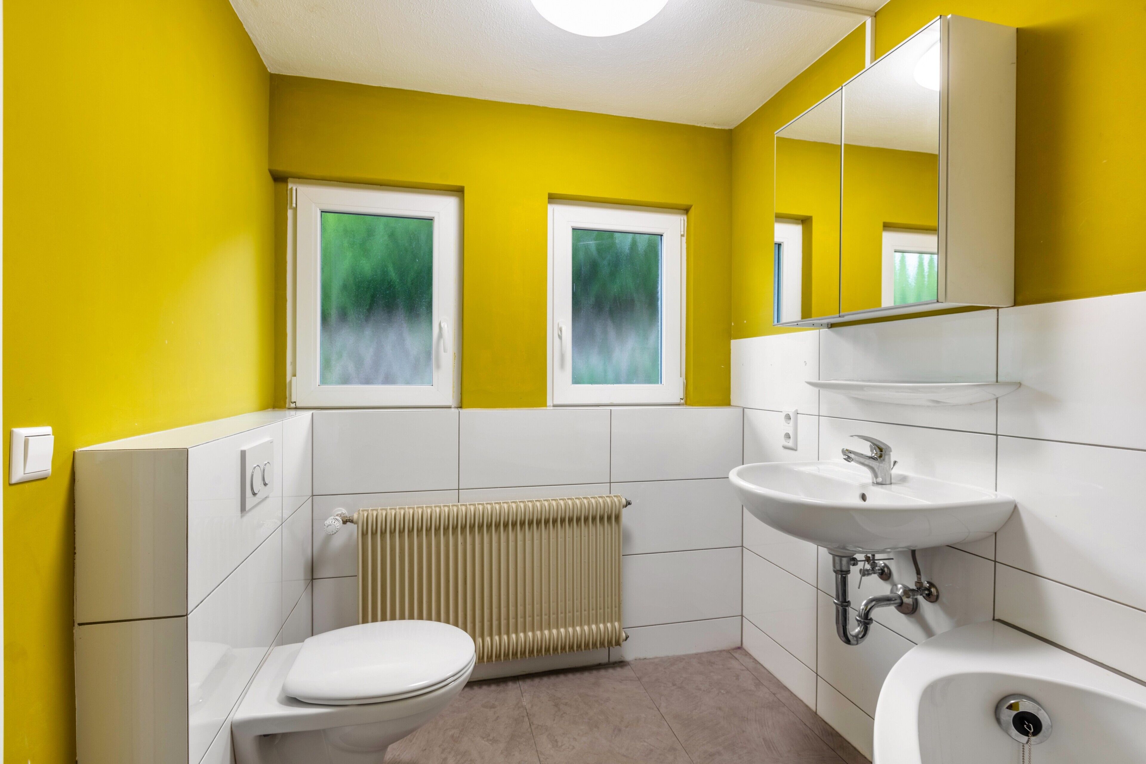 A bathroom with a toilet, a sink, a mirror, and a radiator.