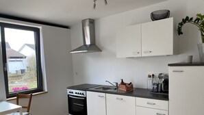 Une cuisine moderne avec des meubles blancs, une cuisinière et une fenêtre donnant sur un jardin.