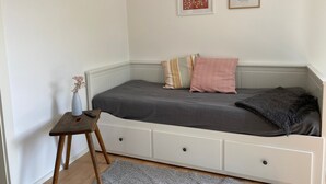 Une chambre à coucher avec un lit, une petite table, un vase et deux tableaux encadrés accrochés au mur.