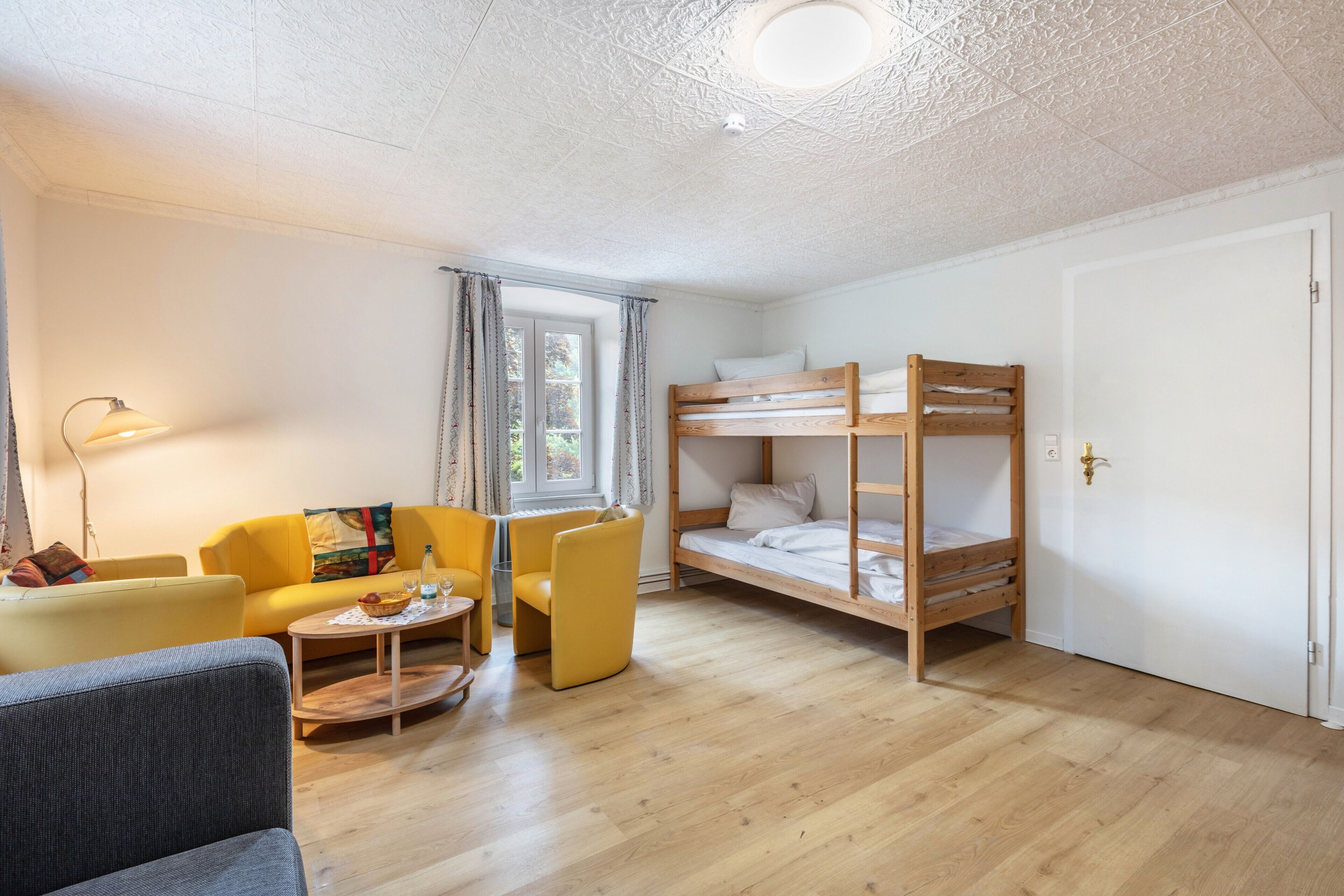 A room with a bunk bed, a sofa, a chair, a small table, and a lamp.