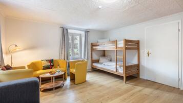 A room with a bunk bed, a sofa, a chair, a small table, and a lamp.