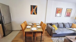 A dining area with a table set for six, a grey sofa with cushions, and a refrigerator.