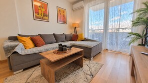 Un salón con un sofá gris, una mesa de centro de madera y un ventanal con cortinas translúcidas.