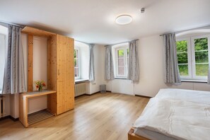 Een slaapkamer met een houten garderobe, een bed, een klein tafeltje met bloemen en een raam met gordijnen.