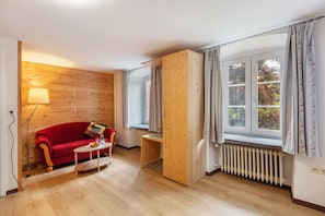 Una habitación con pared de madera, sofá rojo, una mesita, un radiador y una ventana con cortinas.