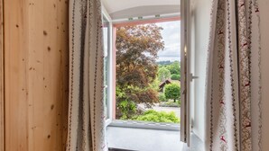 A window with curtains, a radiator below, and a view of trees and a house. - Holiday Apartment 'Vielfalt' with Mountain View, Shared Terrace and Wi-Fi (Elbenschwand)