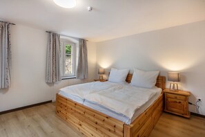 Un dormitorio con cama de madera, dos mesitas de noche con lámparas, una ventana con cortinas y un enchufe.