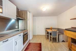 Una cocina compacta con armarios blancos, una estufa de acero inoxidable y una encimera de madera. Hay un comedor con una mesa y sillas, y una alfombra pequeña en el suelo.