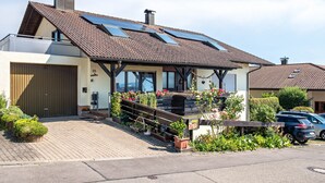 A modern house with a sloped roof, solar panels, a garage, and a garden with potted plants. - Apartment '1' with Private Terrace, Garden and Wi-Fi (Bad Bellingen)