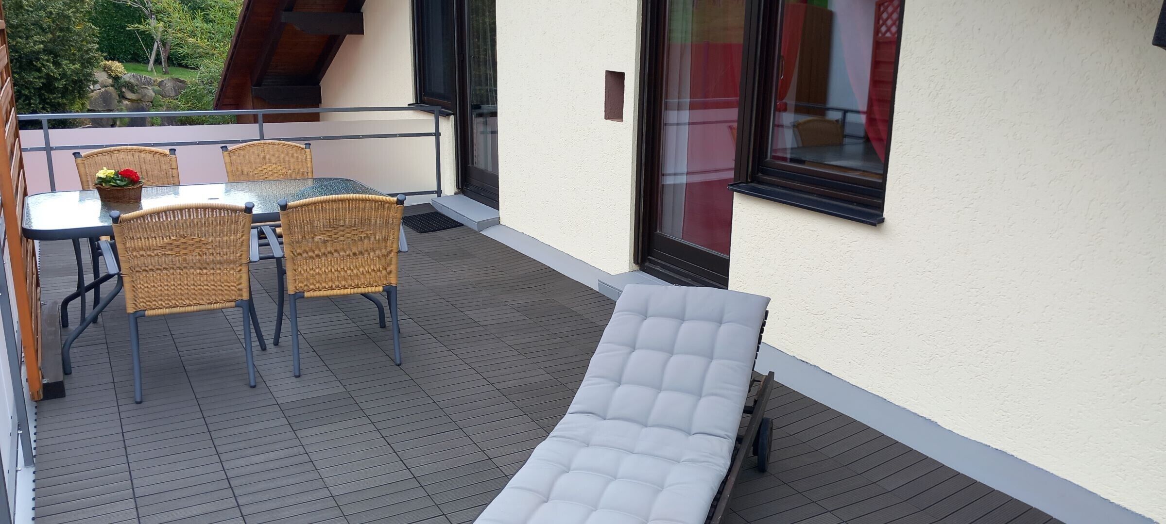 Een balkon met een tafel en stoelen, een comfortabele bank en uitzicht op groen.