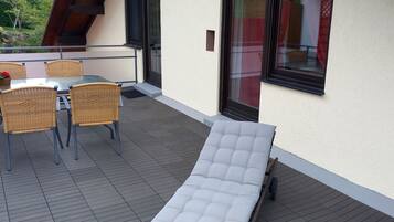 Een balkon met een tafel en stoelen, een comfortabele bank en uitzicht op groen.