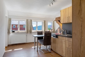 Une cuisine avec des meubles de rangement en bois, une table à manger avec des chaises et une fenêtre avec des rideaux.