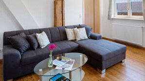Ein modernes Wohnzimmer mit einem Ecksofa, einem Glastisch und einem Holzakzent.