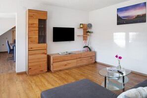 Un salon moderne avec un téléviseur à écran plat, des meubles en bois, une table basse en verre et un tableau accroché au mur.