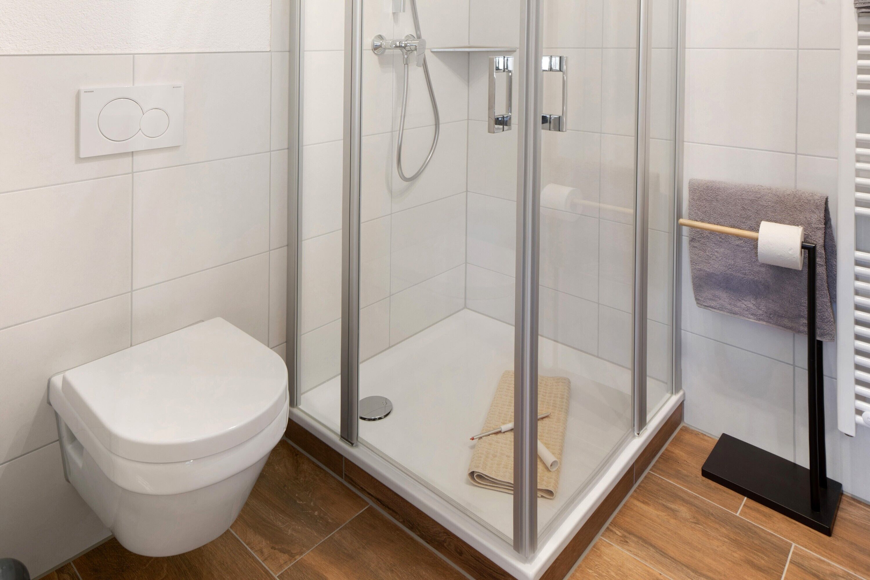 A modern bathroom with a glass-enclosed shower, a white toilet, and a towel rack.