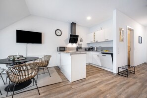 Una cocina moderna con armarios blancos, una campana extractora negra y un comedor con sillas de mimbre y una mesa redonda.