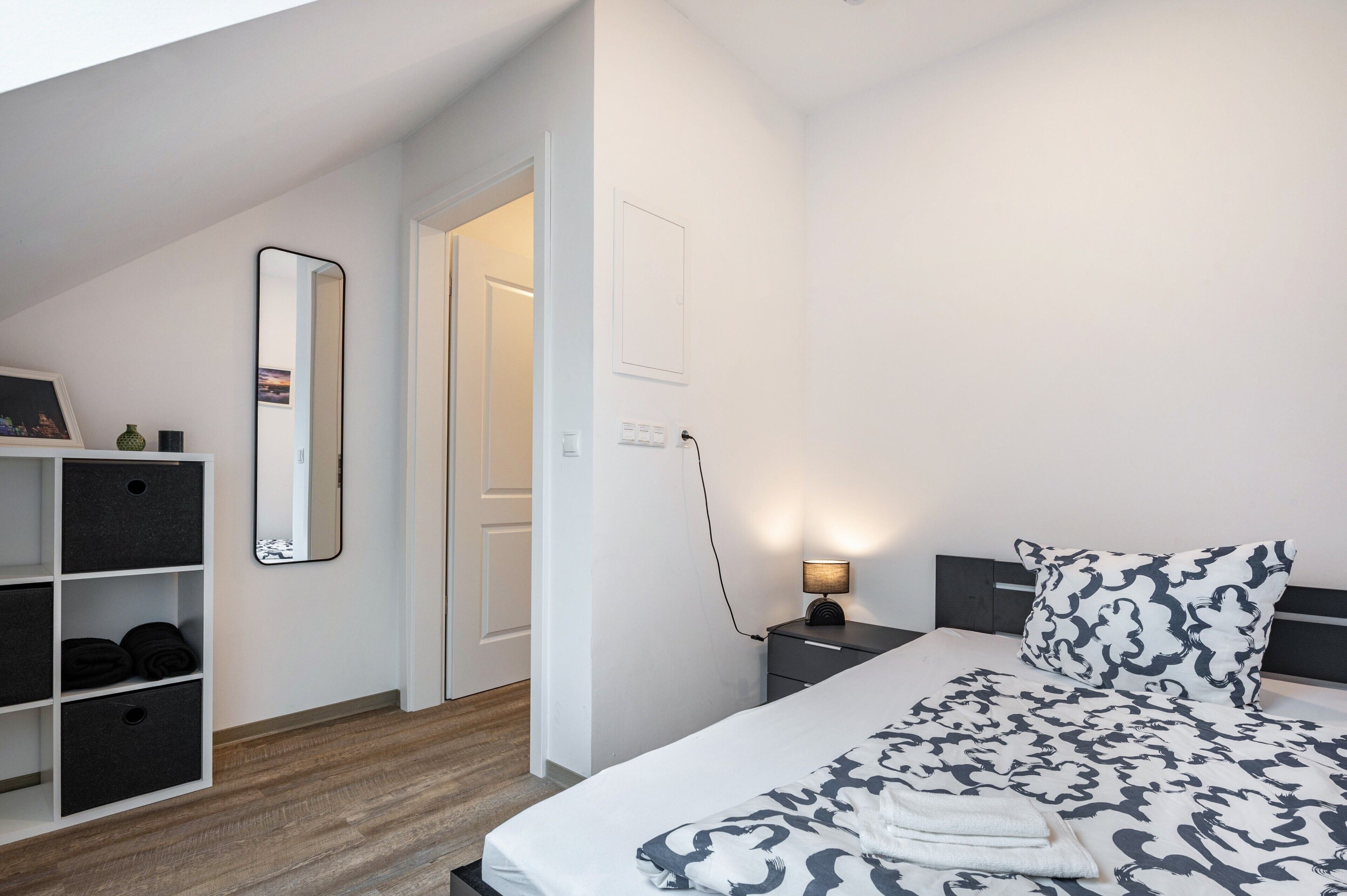 A bedroom with a bed, bedside table, lamp, and storage unit.