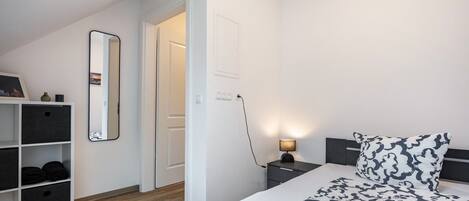 A bedroom with a bed, bedside table, lamp, and storage unit.