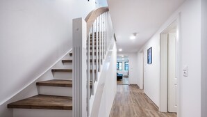 A modern interior with a wooden staircase, white walls, and a hallway leading to a room with a window. - Modern apartment in the city center of Jever (Jever)