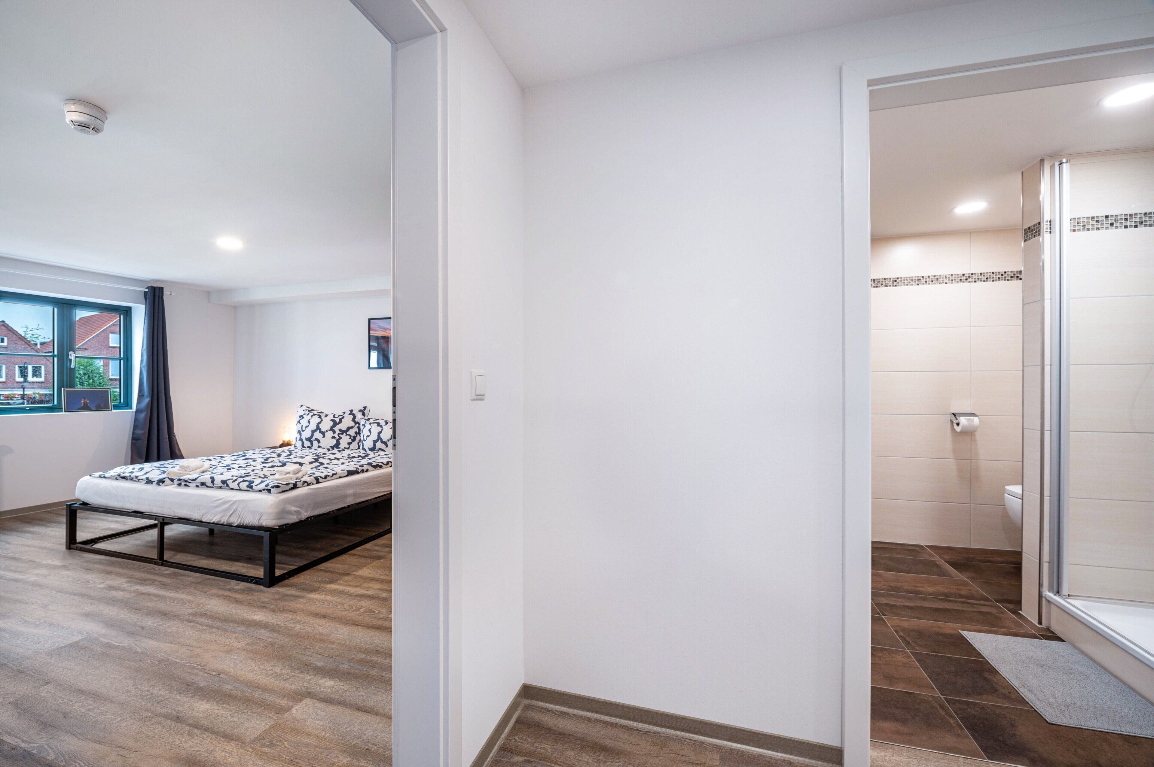 Un dormitori amb un llit, una finestra amb vistes, un bany amb dutxa i una porta que condueix a una altra habitació.